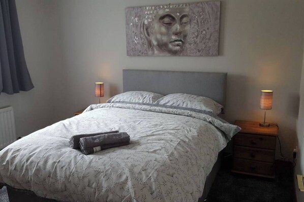 A bedroom with a large bed, two bedside tables with lamps, a headboard, and a wall-mounted artwork.