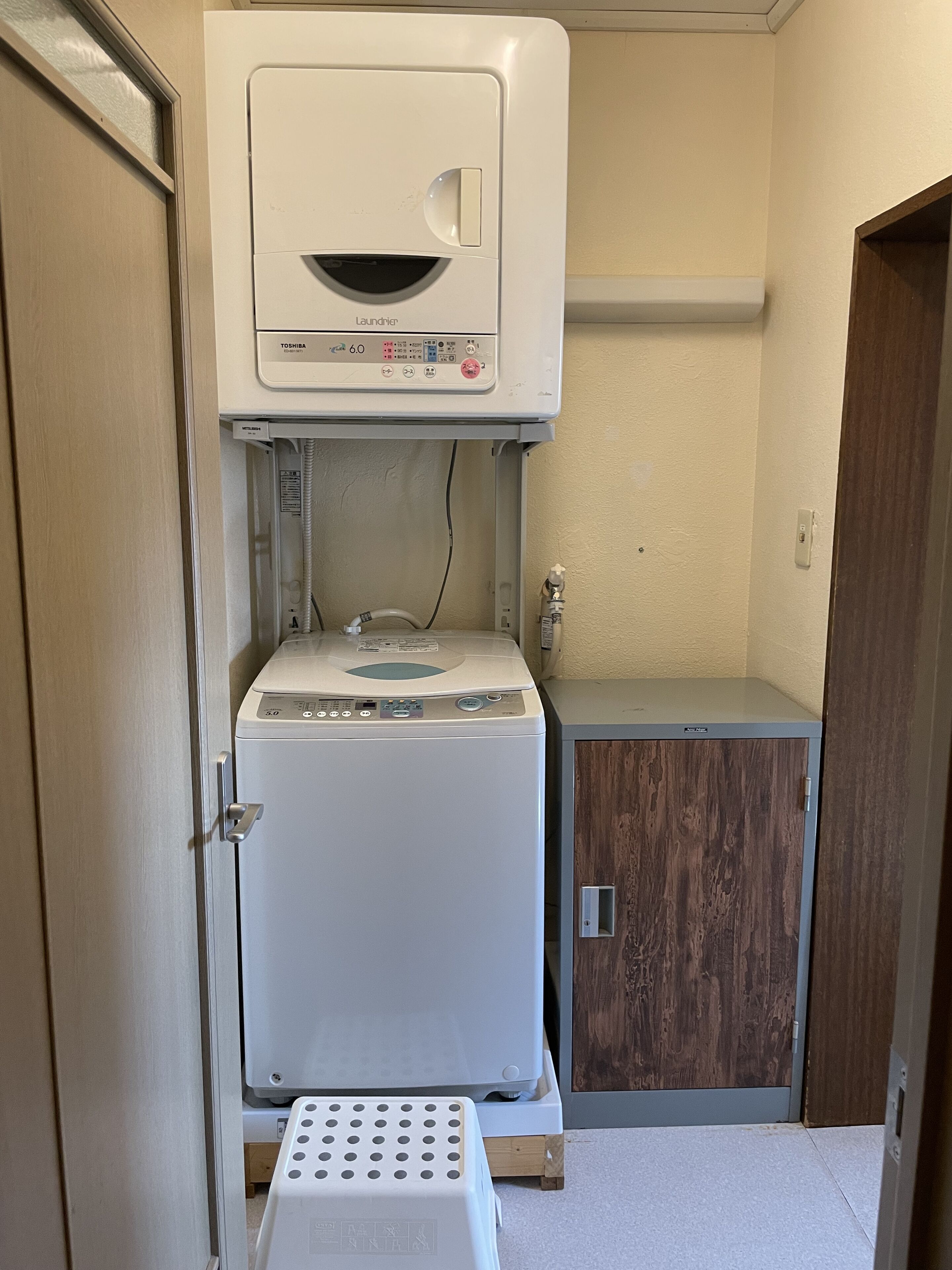 Ein kleiner Waschraum mit einer Waschmaschine mit Frontlader, einem Trockner und einem Schrank.