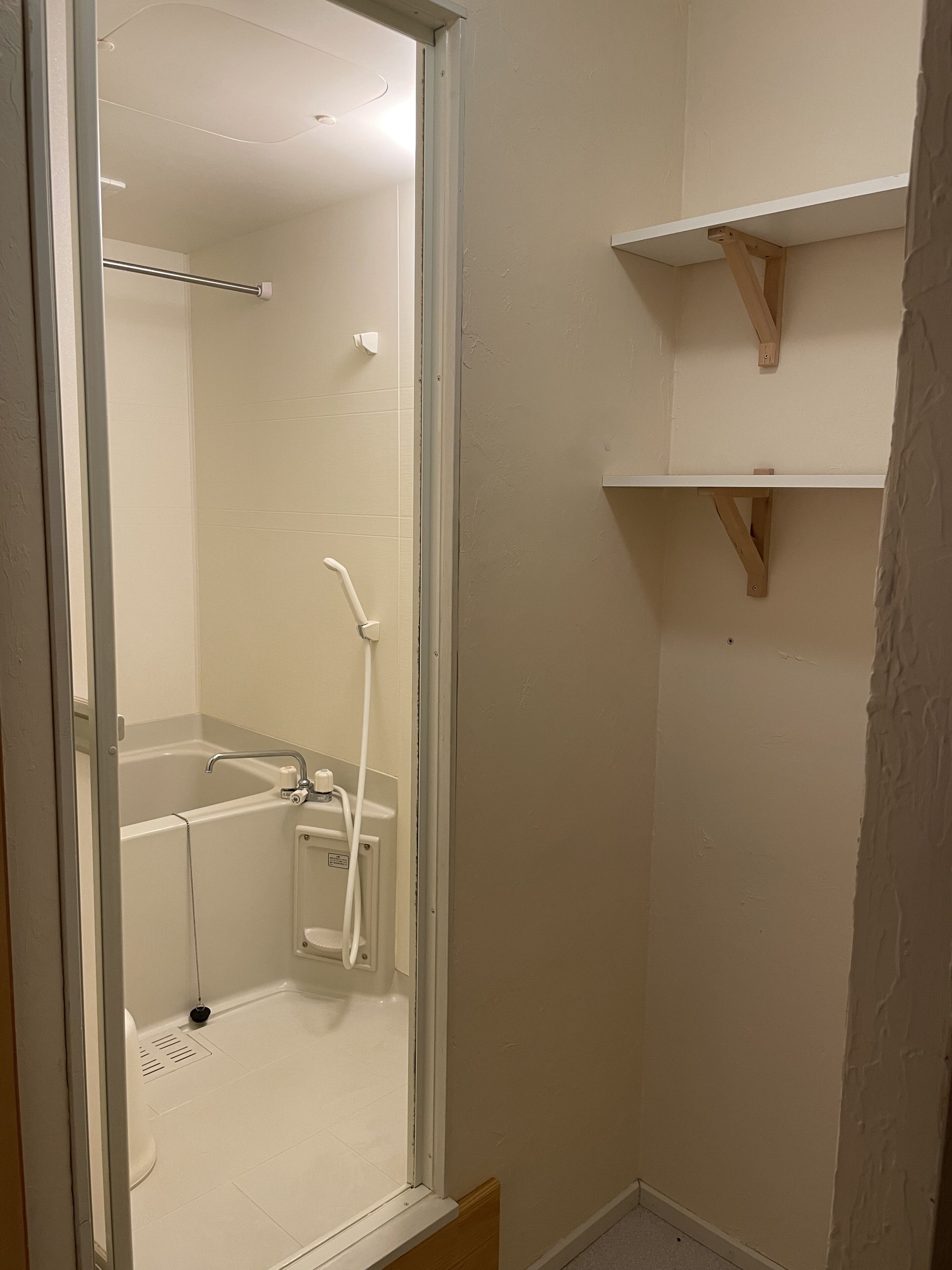 Une salle de bain avec une douche à parois de verre, une baignoire blanche et une petite étagère au-dessus de la baignoire.