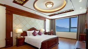 A hotel room with a large bed, wooden headboard, two bedside tables with lamps, a view of the sea, and a ceiling with a circular light fixture. - Sky Beach D20 Nha Trang Hotel (Nha Trang)