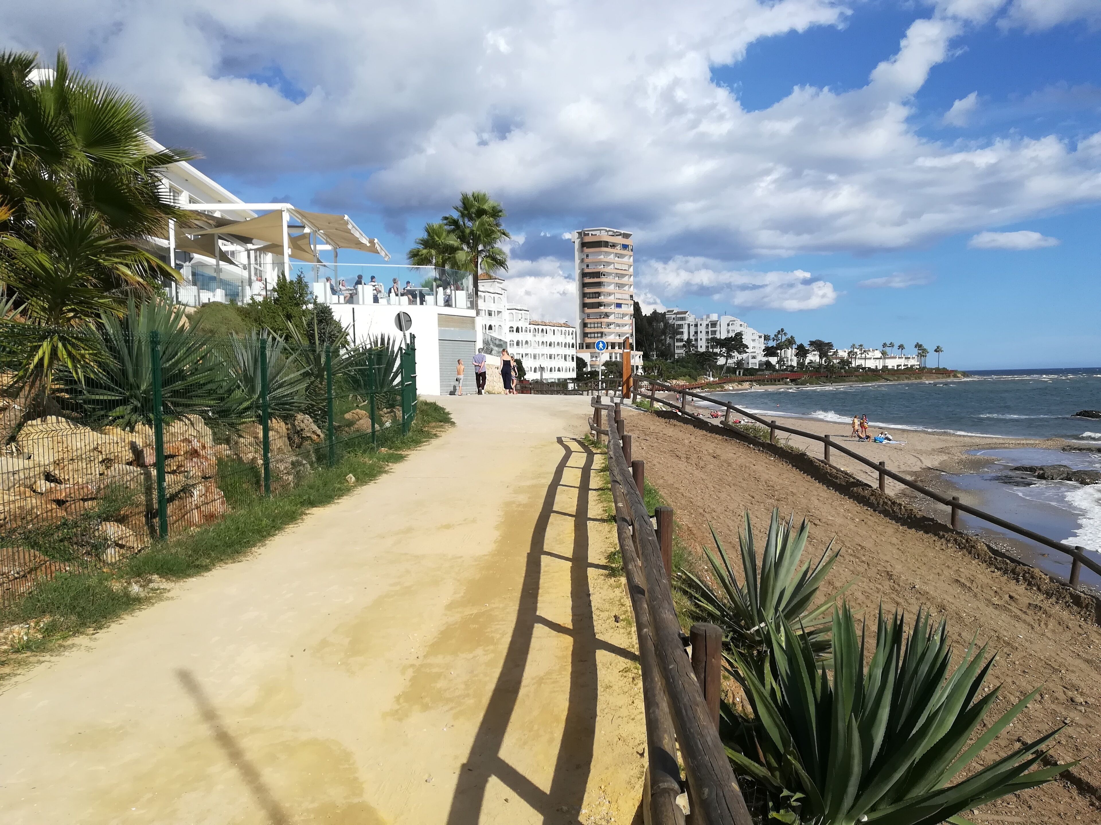 A coastal walkway leading to a beach with a tall building in the background.