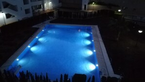 Ein rechteckiger Pool mit blauer Färbung, umgeben von einer niedrigen Mauer und einer Reihe hoher Bäume.