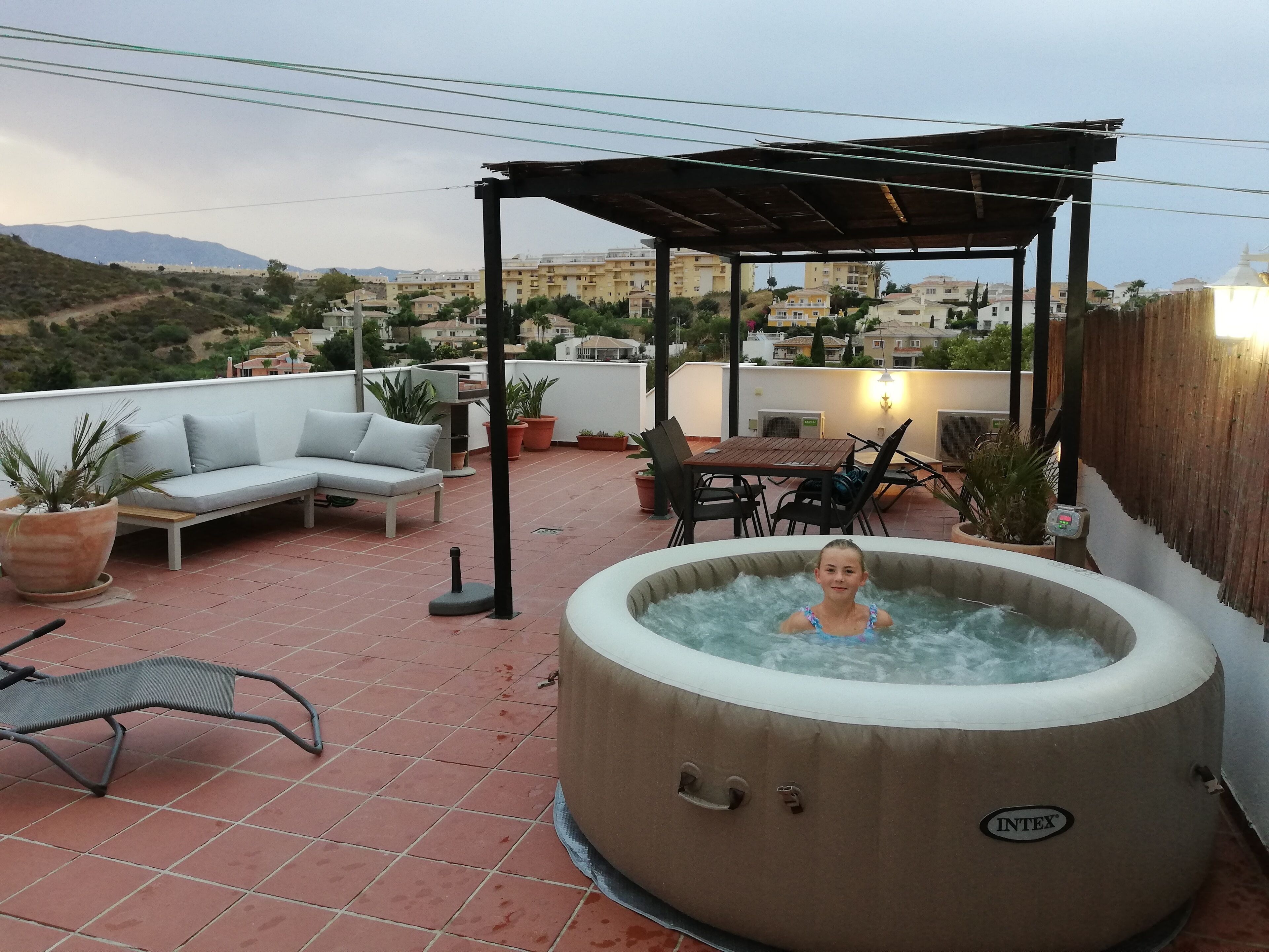 A rooftop terrace with a hot tub, outdoor furniture, and potted plants.