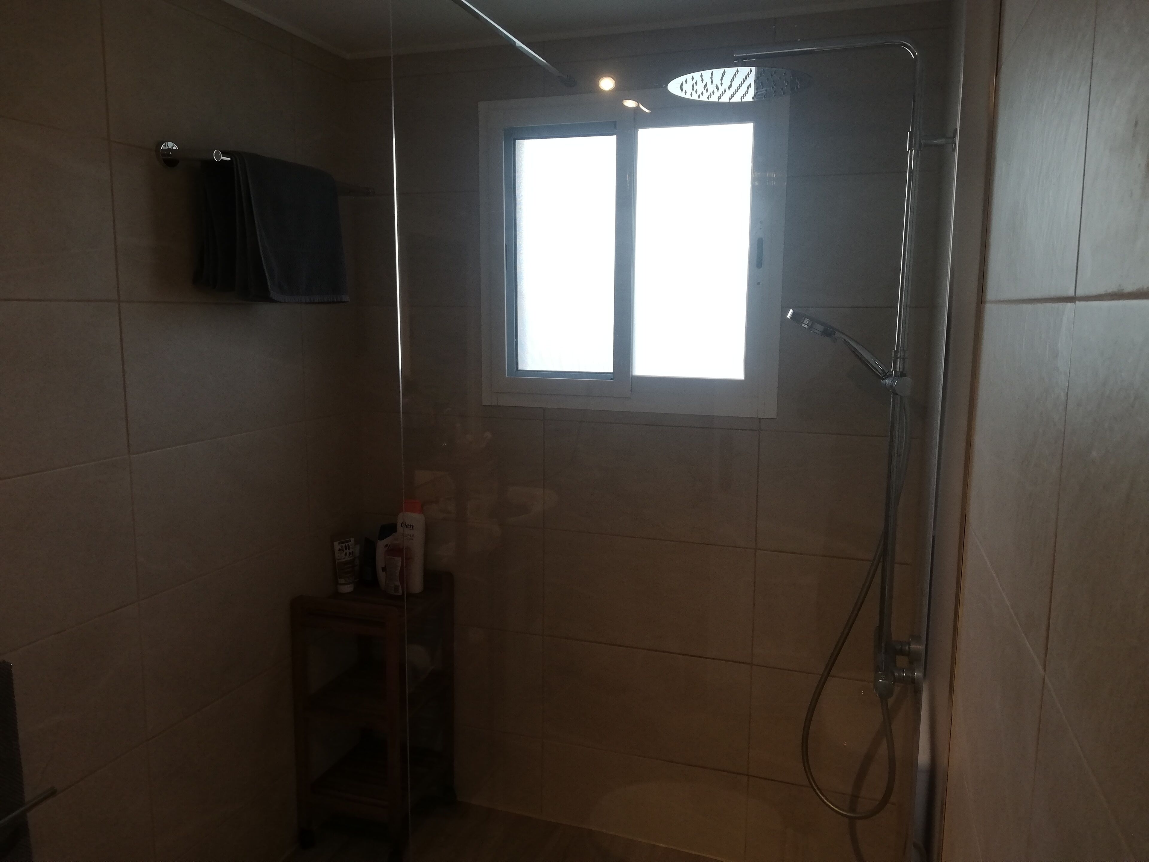 A small bathroom with a shower, a window, and a shelf with toiletries.