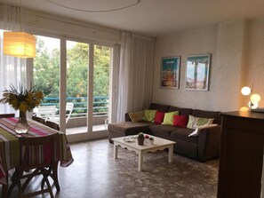 Relax in this inviting living room with a view of lush greenery outside, featuring a comfortable sofa, dining table, and stylish decor.