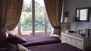 Habitación de hotel con dos camas, un aparador, un espejo y vistas a un balcón con barandilla.