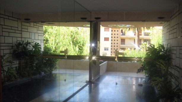 Un espacio interior moderno con una partición de vidrio, suelo de baldosas y plantas en macetas.