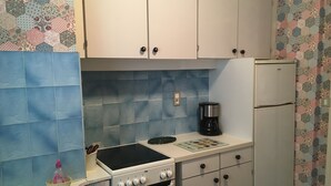 Una cocina compacta con armarios blancos, una cafetera negra y un refrigerador blanco.