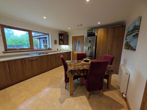 Une cuisine moderne avec des meubles en bois, une table à manger recouverte d’une nappe à motifs floraux et un réfrigérateur.