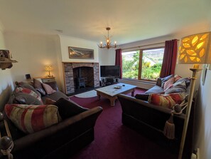 A living room with a fireplace, sofas, a TV, and a large window with a view.