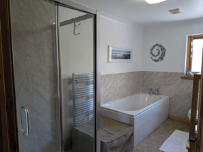 A bathroom with a glass shower door, a bathtub, a towel rack, a framed picture on the wall, and a small window with a view.