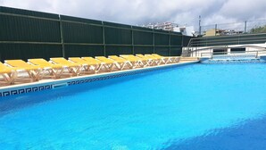 En swimmingpool med gula solstolar och ett grönt staket.