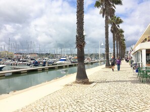 A marina with boats docked, a cobblestone walkway, and palm trees lining the path. - LAGOS apartment *Pool, Wifi, Aircon etc* Close to the beach and Marina! (Lagos)