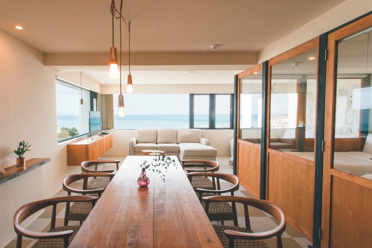 A modern dining area with a wooden table, chairs, and a view of the ocean.