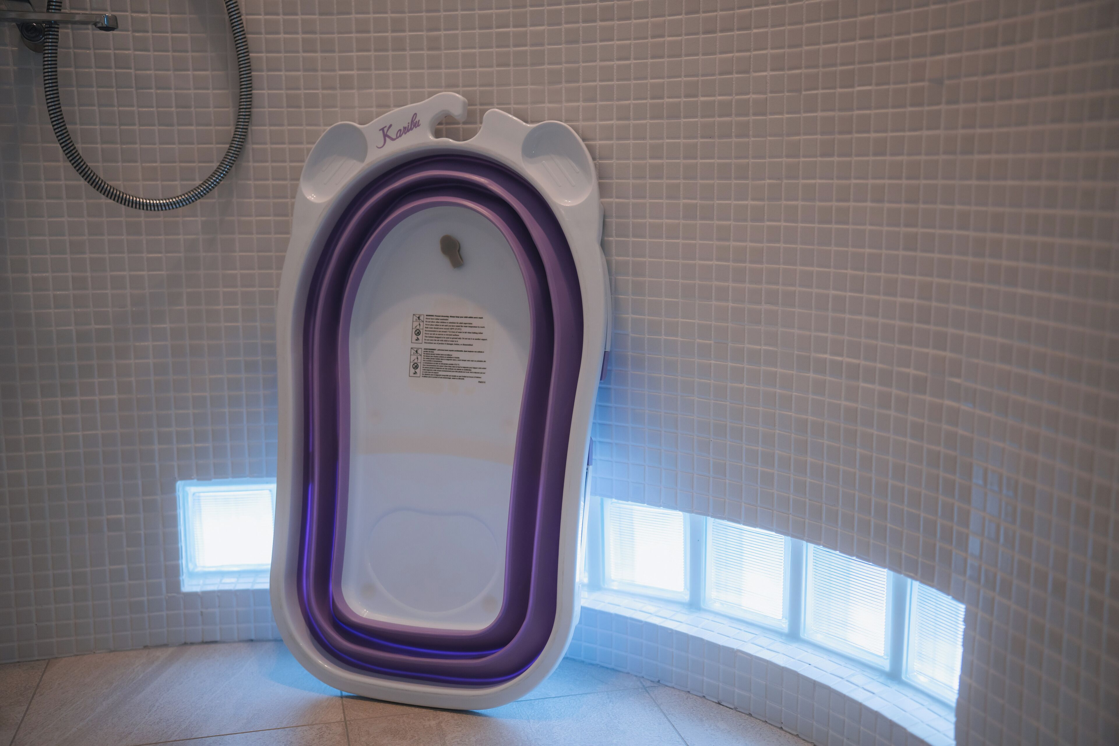 A modern bathroom with a white and purple bidet, tiled walls, and a window providing natural light.