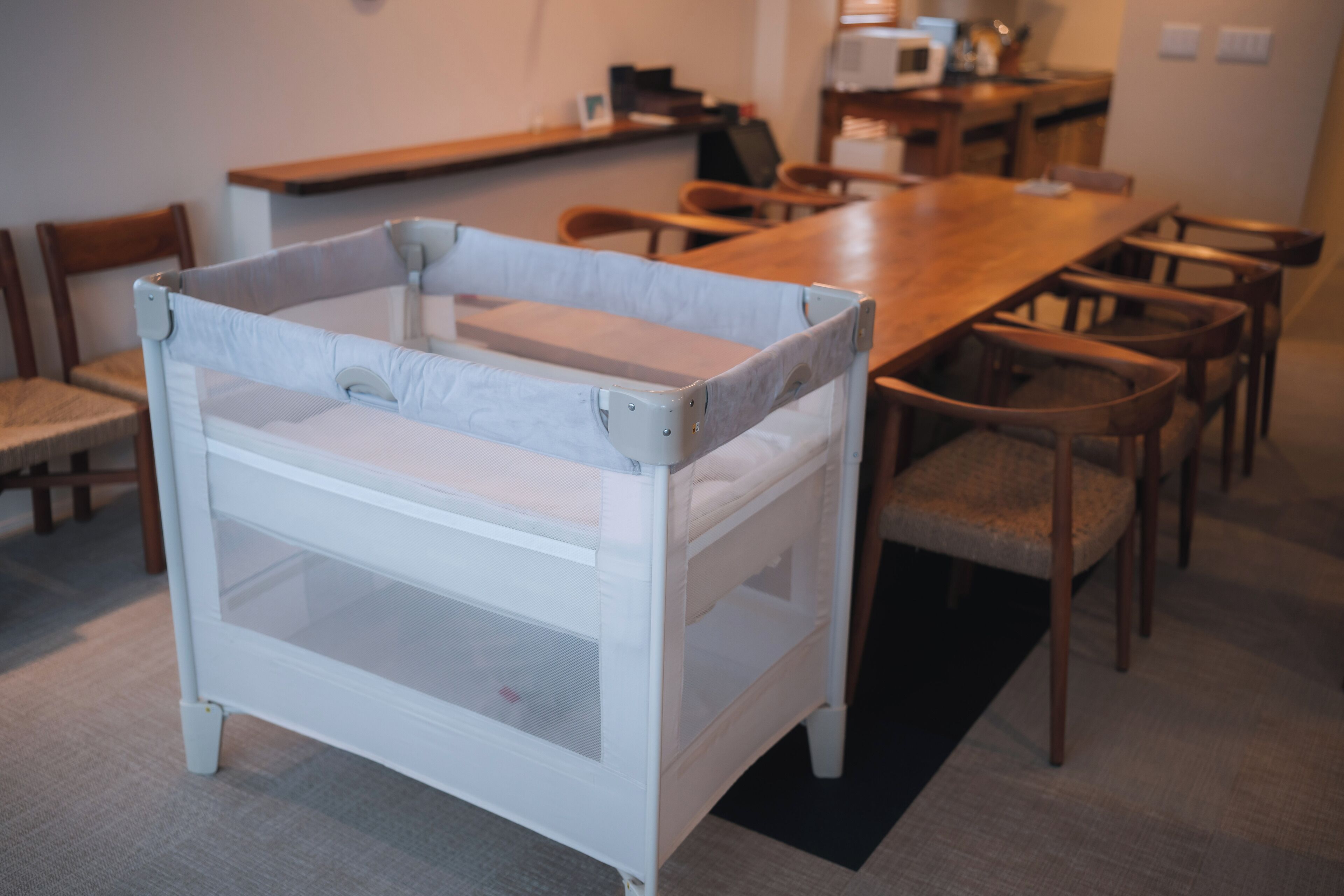 A room with a white crib, wooden dining table, and chairs.