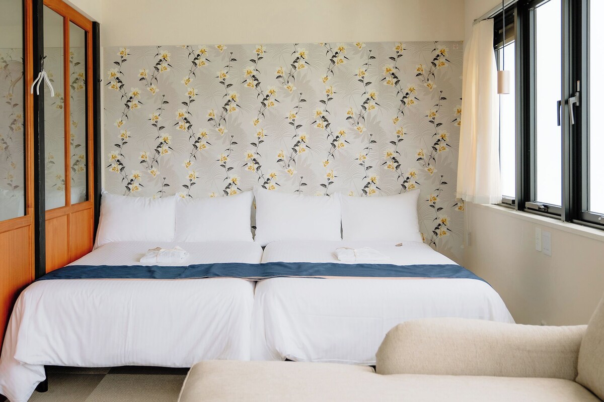 Ein Hotelzimmer mit Bett, zwei Kissen, einer blauen Decke, einem Holzschrank und einem Fenster mit Blick.
