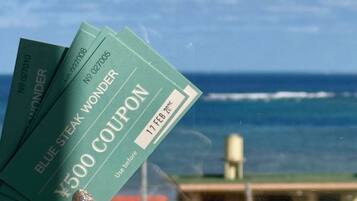 A hand holding three blue coupons with the text "Blue Steak Wonder" and "¥500 Coupon" against a backdrop of a building and ocean view.