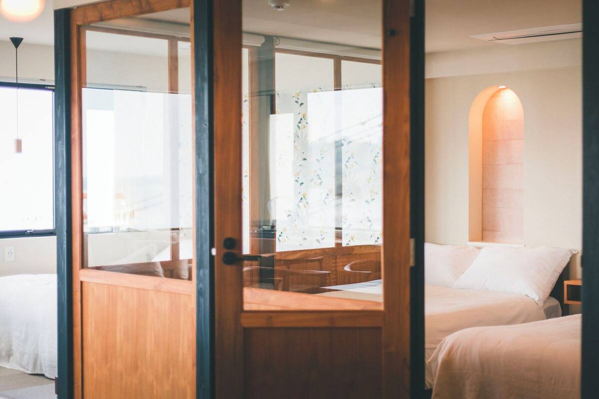 A hotel room with a wooden desk, two beds, and a large window with a view.