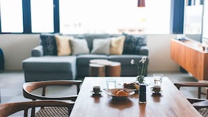 Un coin repas avec une table en bois, des chaises, une assiette de nourriture, un verre d’eau et un vase rempli de fleurs.