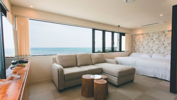 Une chambre d’hôtel moderne dotée d’une grande fenêtre donnant sur la mer, d’un canapé, d’un lit et d’une petite table en bois.