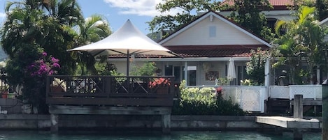 A waterfront property with a white building, a covered area with a white canopy, and lush greenery.