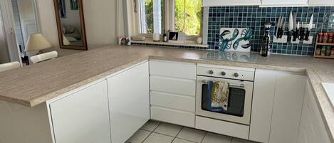 A kitchen with white cabinets, a tiled backsplash, and a window with curtains.