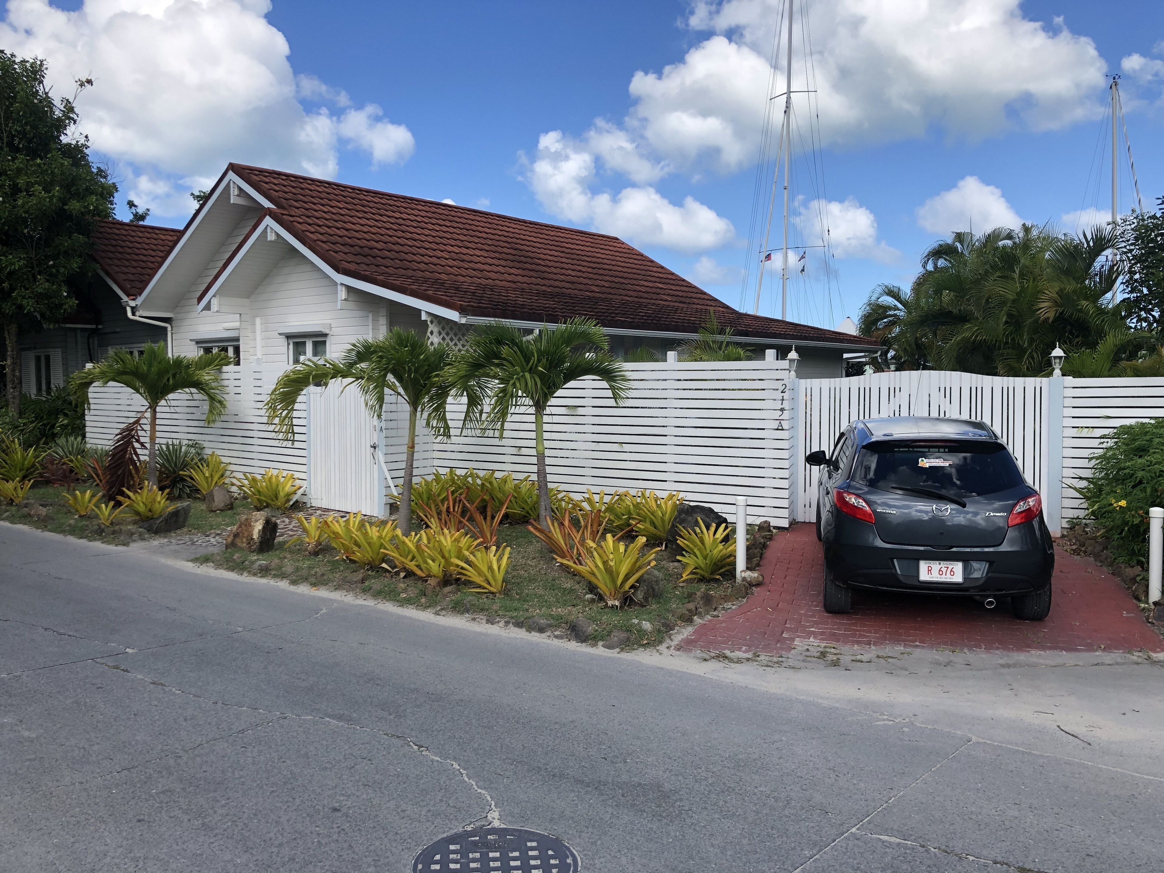 A residential house with a red-tiled roof, a white fence, and a parked car.