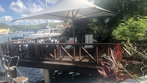 Eine Holzterrasse mit Baldachin, mit Blick auf einen Yachthafen mit Booten und Grünflächen.