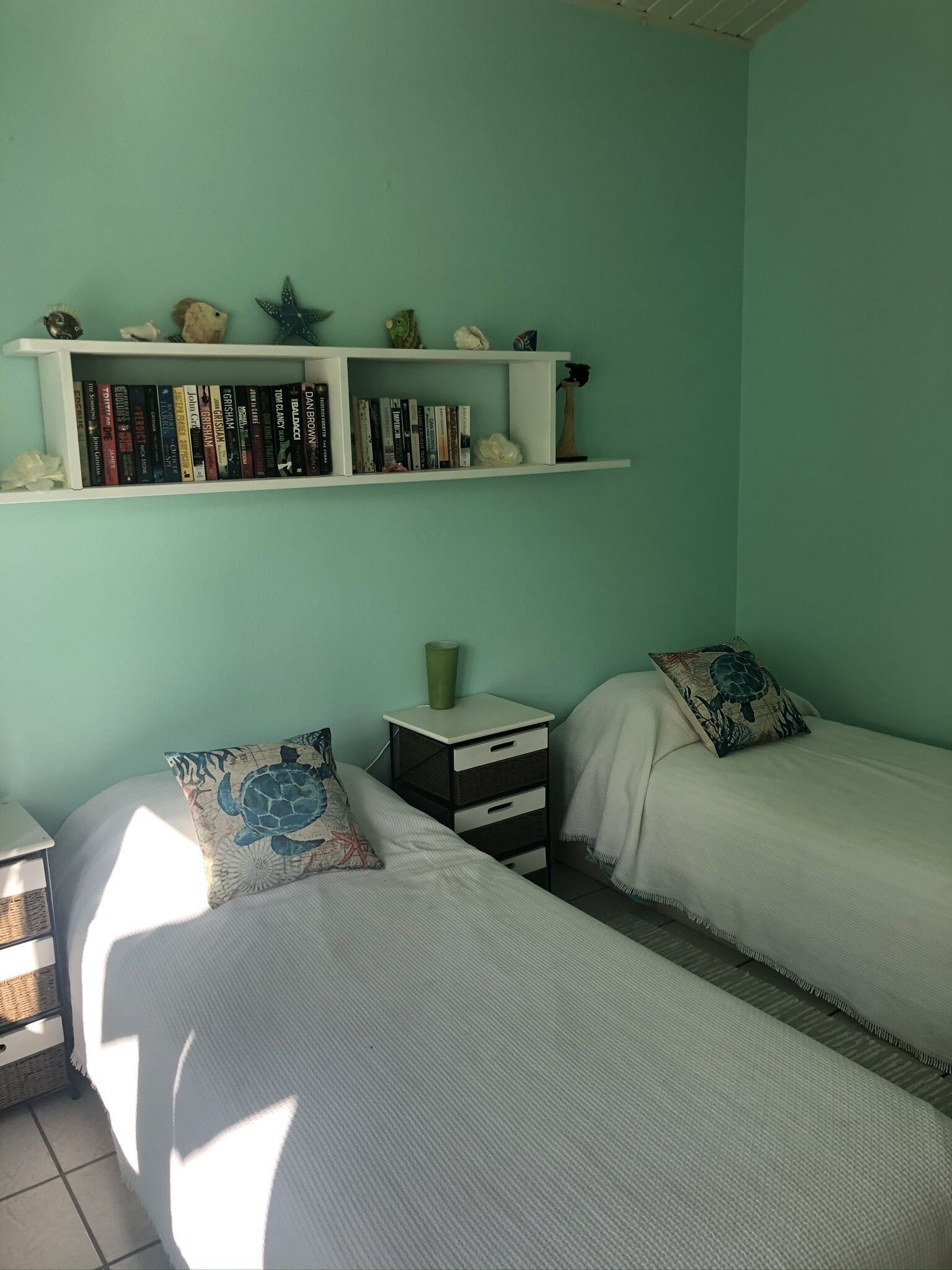 A bedroom with two single beds, a nightstand, a bookshelf, and a window.