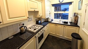 A kitchen with white cabinets, a gas stove, a sink, and a window with a view.