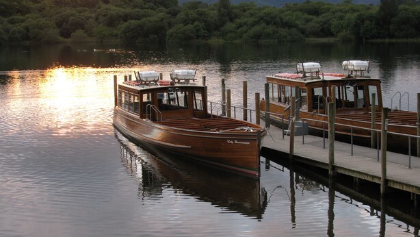 A wooden boat docked at a pier with a cabin and lifeboats.