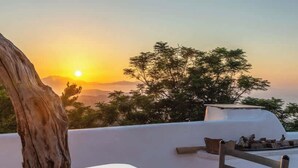 A terrace with a white table, a chair, and a view of the sunset over the sea.