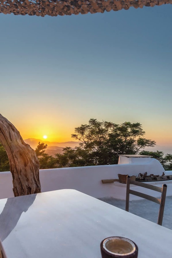 A terrace with a white table, a chair, and a view of the sunset over the sea.