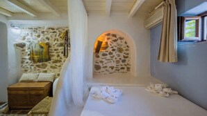 A stone-walled room with a small arched window, a wooden bench, and a bed with towels.