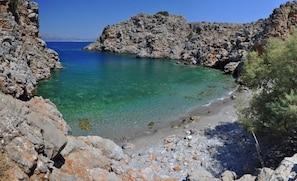 A rocky coastline with clear turquoise water, a pebbly beach, and rugged cliffs.