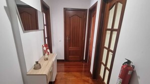 A hallway with wooden flooring, a wooden door at the end, and a fire extinguisher mounted on the wall. - Terrace Garden Apartment  (Funchal)