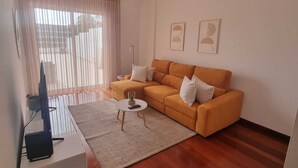 A modern living room with a sofa, a coffee table, and a TV on a stand. - Terrace Garden Apartment  (Funchal)