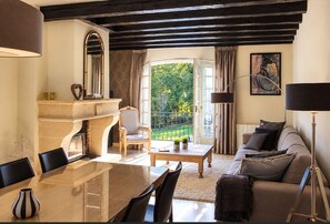A room with a fireplace, a dining table, a sofa, and a view of greenery outside.
