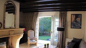 A living room with a fireplace, a sofa, a coffee table, and a view of the garden through an open door.