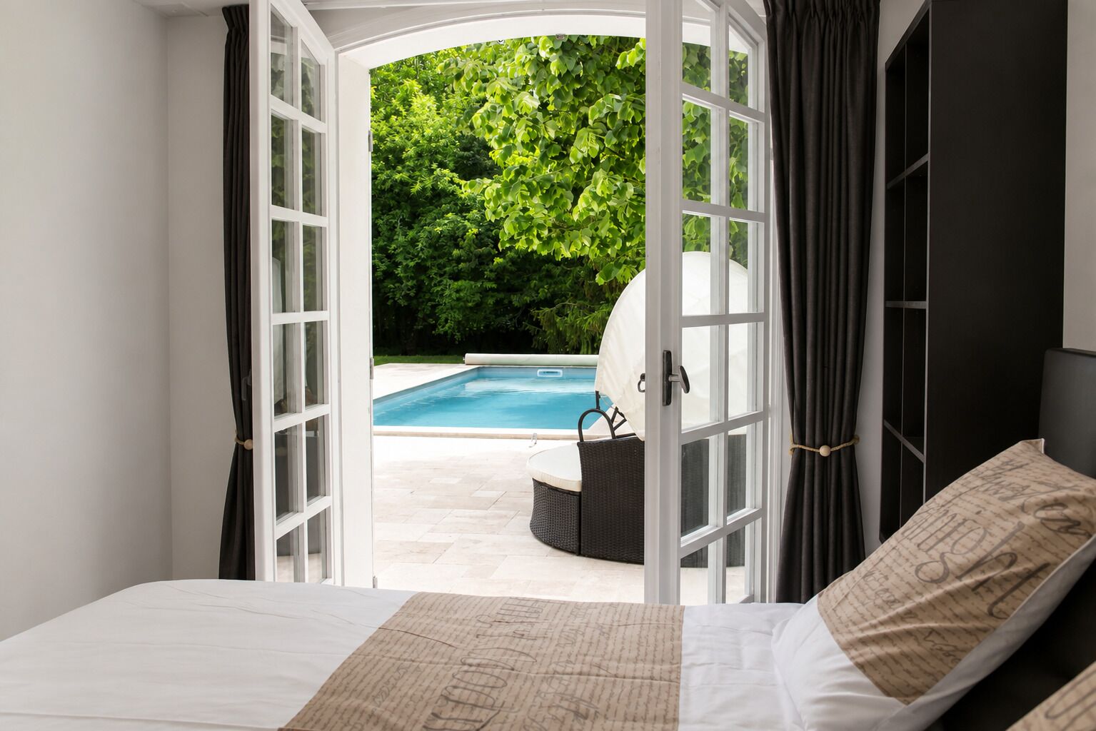 Une chambre avec vue sur une piscine, un lit et un fauteuil.