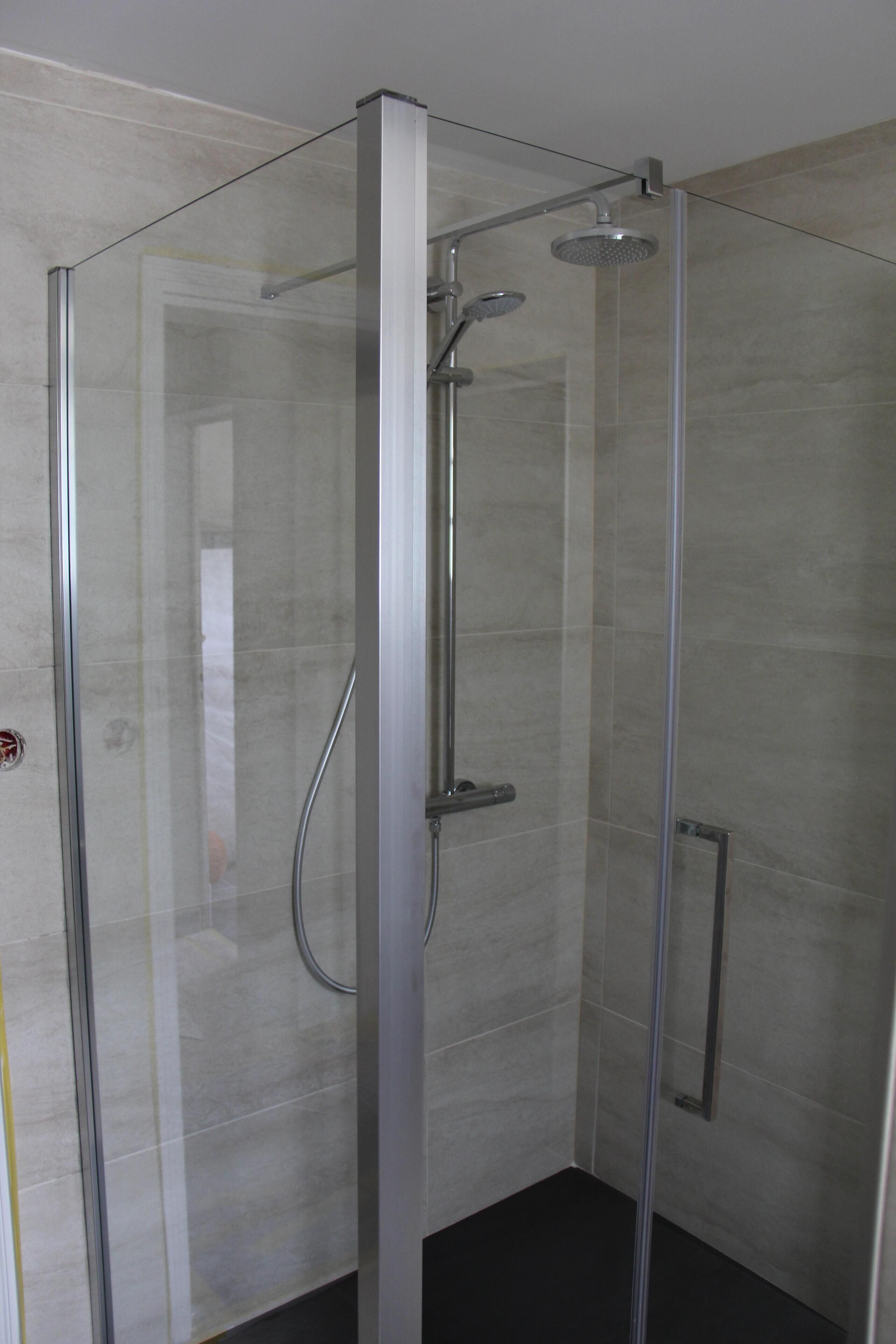 A glass-enclosed shower with a handheld showerhead and a wall-mounted faucet.