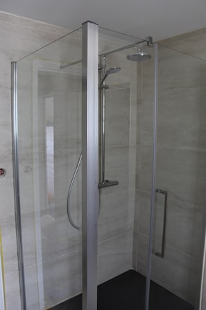 Una ducha con cerramiento de vidrio, cabezal de ducha de mano y grifo empotrado.