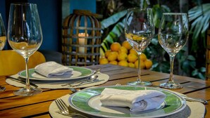 A table set with plates, cutlery, and wine glasses, with a basket of oranges in the background. - Secret garden iguazu (Puerto Iguazú)