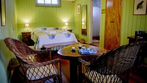 A room with a bed, two bedside tables with lamps, wicker chairs, a small round table with a tray, and a wooden door. - Secret garden iguazu (Puerto Iguazú)