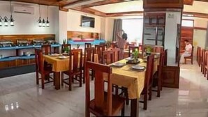 A spacious dining area with multiple tables and chairs, a kitchen area with counters and appliances, and a view of the outdoors through large windows. - NuttyPhoy Hotel (Vang Vieng)