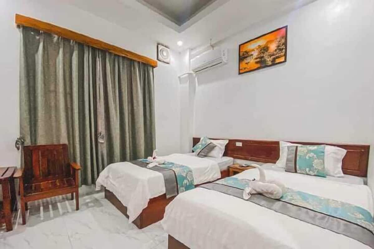 A hotel room with two beds, a wooden chair, a large window with curtains, an air conditioning unit, and a painting on the wall.