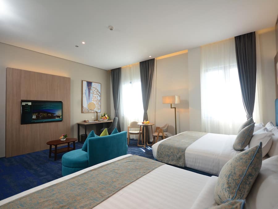 Une chambre d’hôtel avec deux lits, un bureau avec une chaise, une télévision et une petite table avec une lampe.