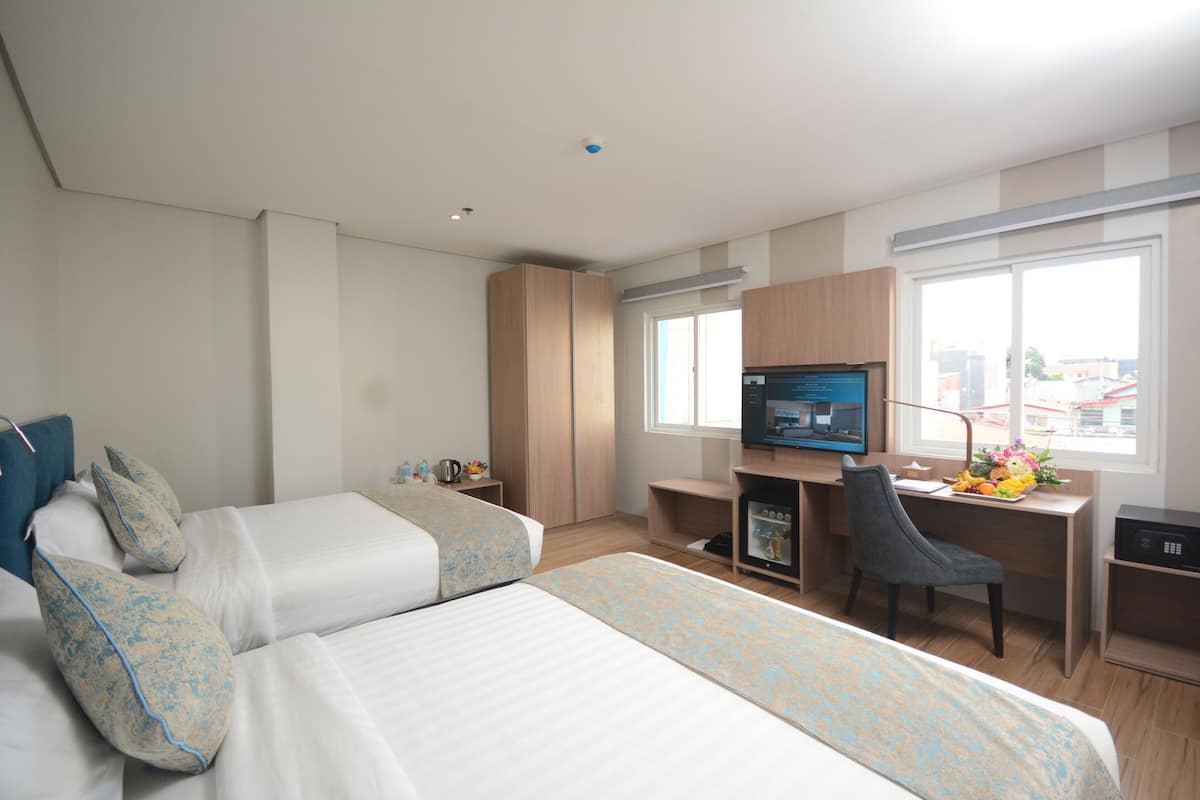 A hotel room with two beds, a desk, a chair, a TV, and a window.