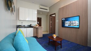 A hotel room with a blue sofa, a small wooden table with a flower vase, a television on the wall, and a kitchenette in the background. - Blue Lotus Hotel Davao (Davao)